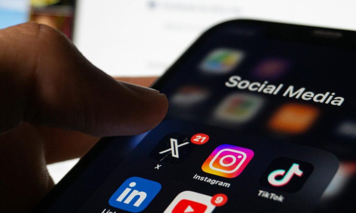 phone screen showcasing various social media icons with a laptop open on the instagram login screen in the background