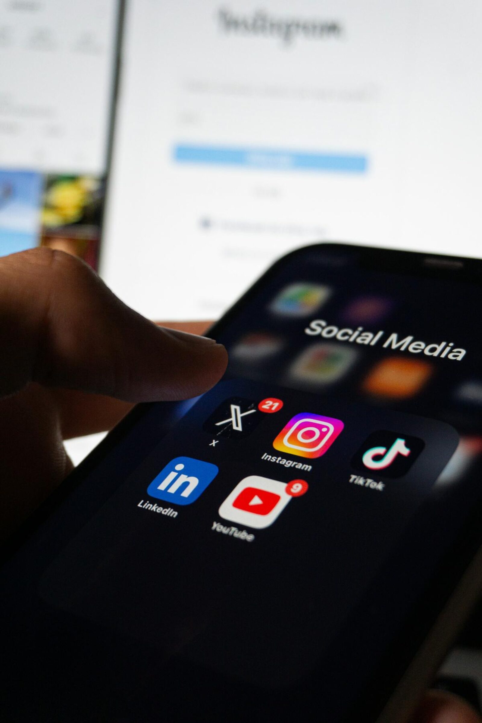 phone screen showcasing various social media icons with a laptop open on the instagram login screen in the background