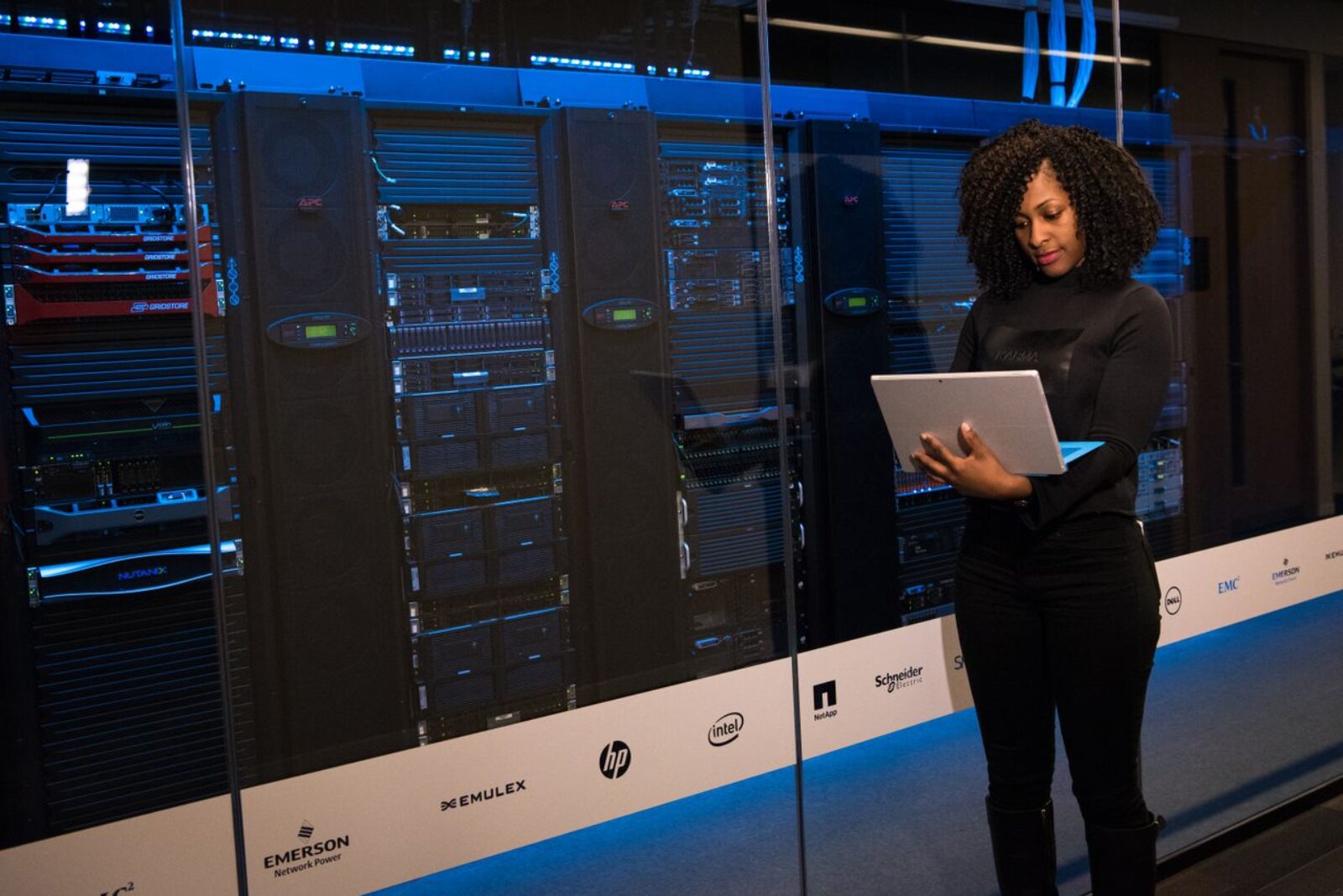A female IT professional using a laptop while monitoring data servers in a server room illustrating server management
