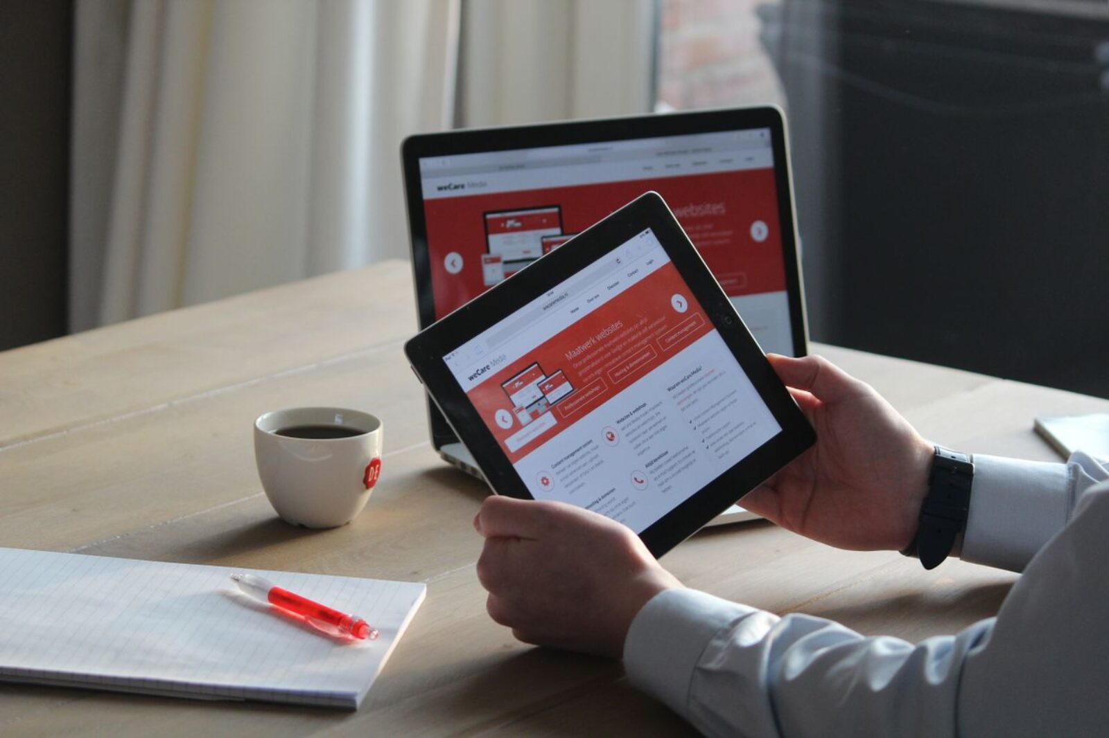 Business professional using a tablet and laptop with a hot drink, focusing on digital content review illustrating the process before a website rebuild